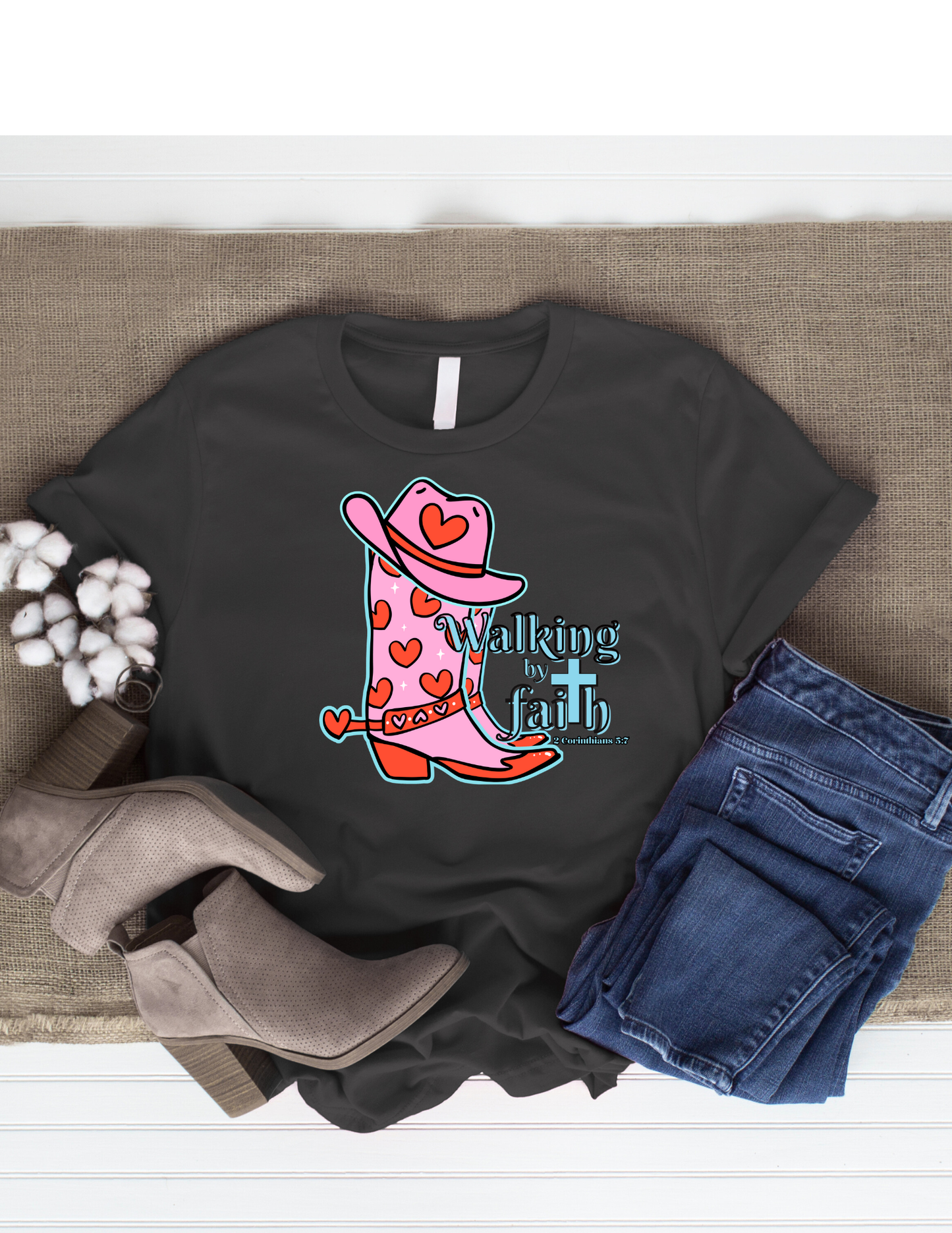 Black t-shirt with pink cowboy boot graphic and 'Walking by Faith' text, paired with jeans and boots on a textured surface.