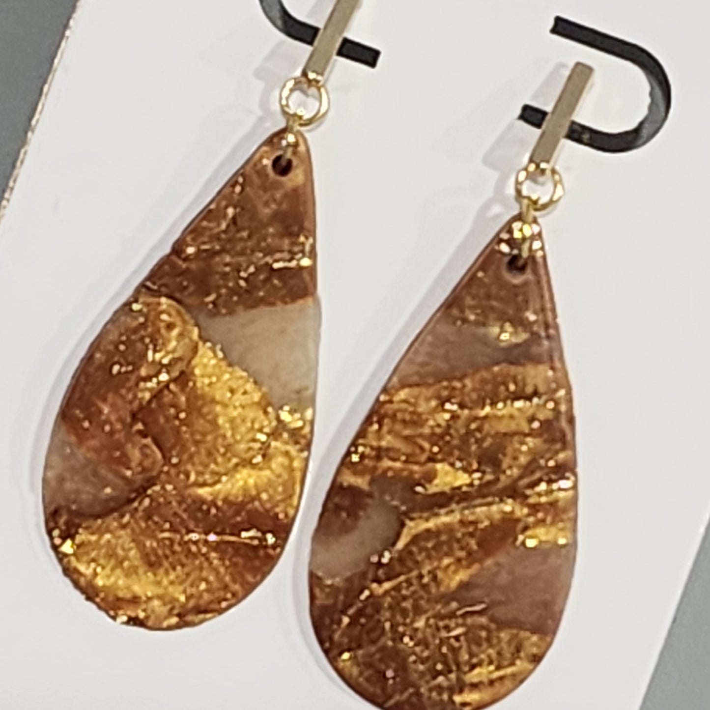 Gold and bronze teardrop earrings on a white card